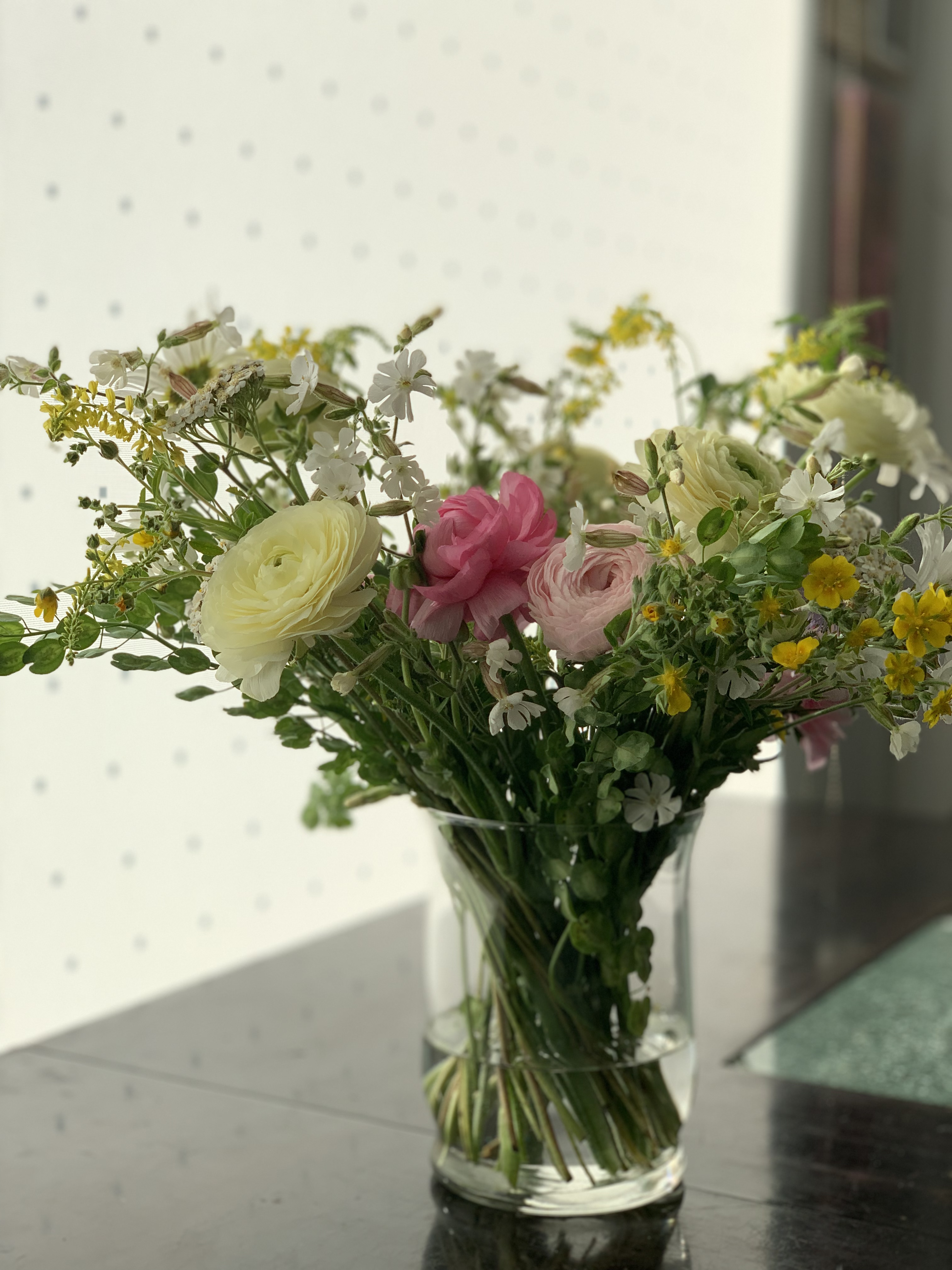 Mixed bouquet of ranunculus, daisies, and yarrow in a glass vase.