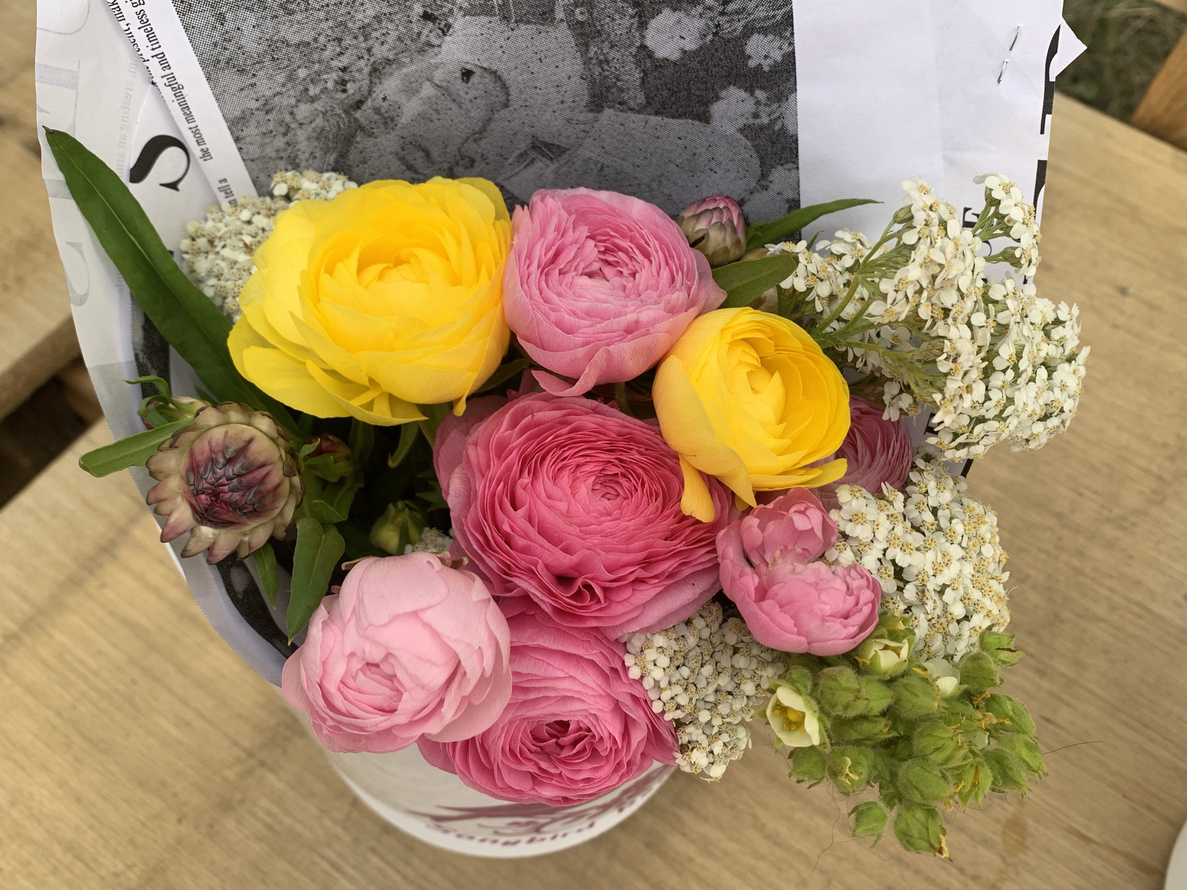 A colourful wrapped bouquet of ranunculus, strawflower, potentilla, and yarrow.